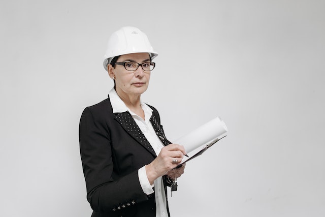 property inspector in a suits wearing a white hardhat and carrying a clipboard